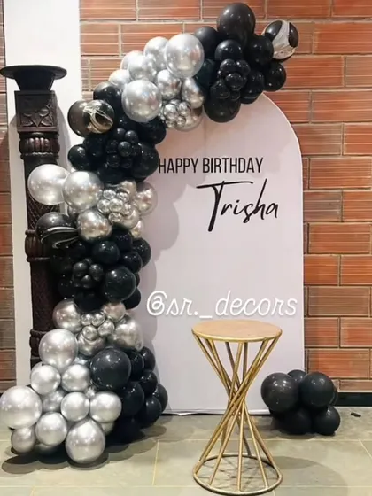 A minimalist and chic backdrop for an 18th birthday, with a personalized sign and a stylish black and silver balloon garland.