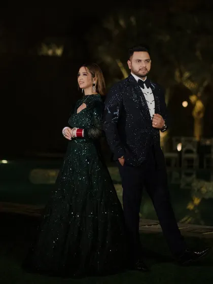 A stylish portrait of the couple at their outdoor reception. Dressed in glamorous evening wear, they pose back-to-back, exuding confidence and elegance.