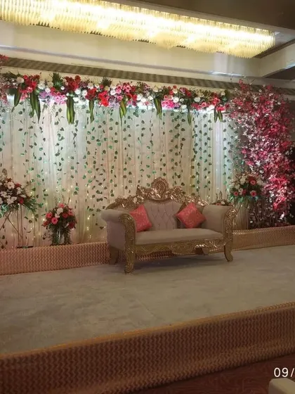 A beautiful reception stage setup with a backdrop of fairy lights and cherry blossom trees. The design is simple yet elegant, with a classic sofa for the couple.