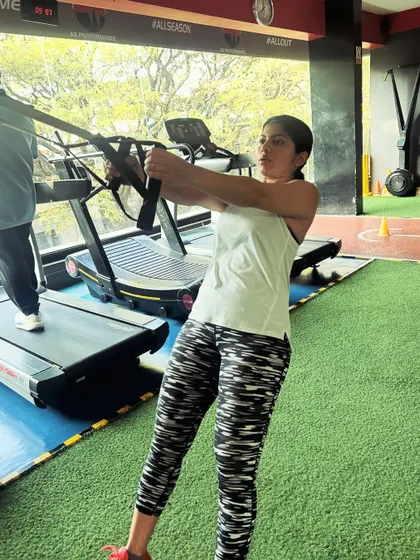 A client uses a cable machine for a standing row, focusing on her back and core muscles.