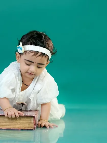 A simple and beautiful portrait of a baby girl with a book, taken against a clean studio background.