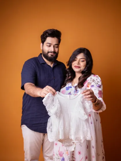 Holding up a tiny dress, dreaming of the little one who will soon wear it. This is a beautiful way to make the dream of your baby feel so real during your couple's maternity session.