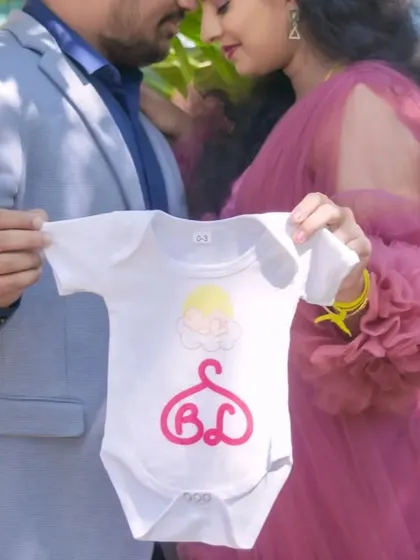 A creative announcement photo focusing on a baby onesie with custom initials. This is a unique and personal way for a couple to share their excitement.