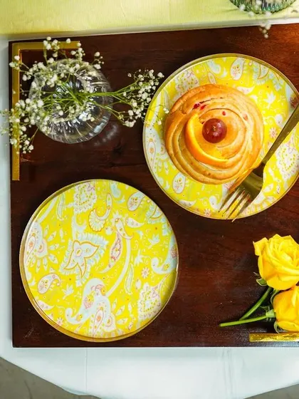 A top-down shot of a breakfast tray with two yellow plates, one empty and one with a pastry. The composition is balanced and aesthetically pleasing.
