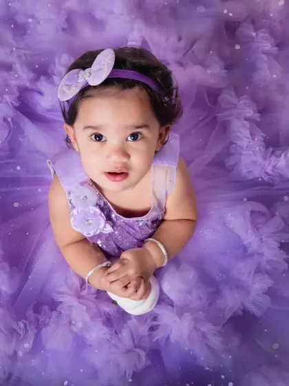A stunning top-down portrait of a little girl in a fluffy purple dress, looking up with wide, curious eyes.