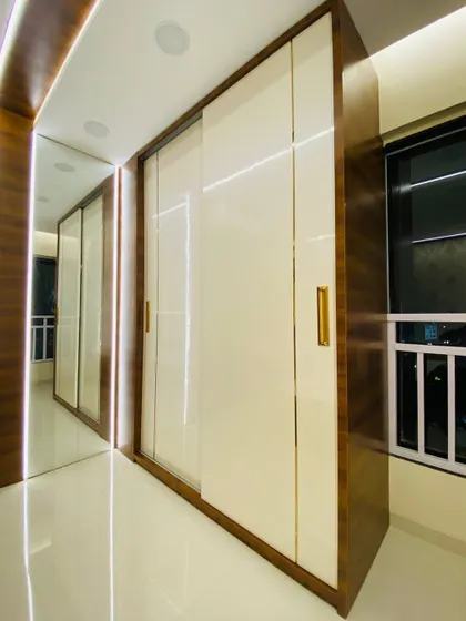 The sliding doors of the wardrobe are closed in this shot, showing the clean and seamless look. The combination of high-gloss white and dark wood is a timeless classic.