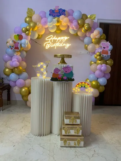 A pastel and gold Peppa Pig themed third birthday party. This elegant setup includes a circular balloon arch, a neon sign, and decorative props.