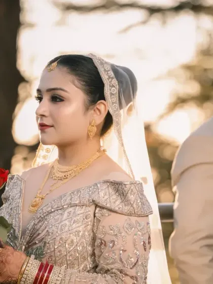 A beautifully composed portrait with the bride in the foreground holding a rose, and her partner slightly out of focus behind her, all bathed in warm sunset light.
