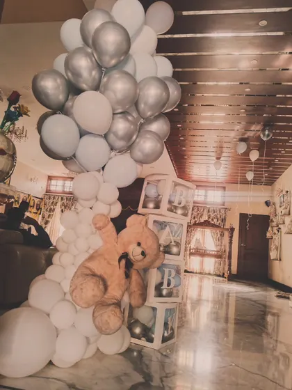 A 'Welcome Baby' decoration featuring a large teddy bear climbing a column of white and silver balloons next to 'BABY' blocks.