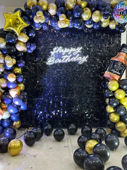 A fun and bold birthday backdrop for a whiskey lover. The black sequin wall is decorated with a black and gold balloon arch and a large whiskey bottle foil balloon.