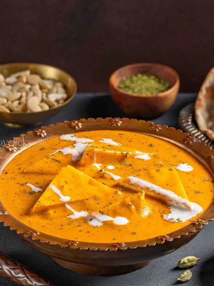 Shahi Paneer in a creamy, orange gravy, garnished with a swirl of cream and styled with a lantern for a royal touch.