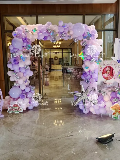 A beautiful lavender and silver balloon arch creates a magical entrance for a fairy-themed party, accented with butterfly cutouts and whimsical mushroom props.