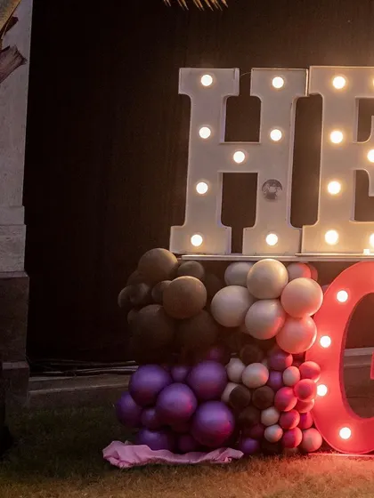 Large marquee letters spelling 'HERE WE GLOW', a popular catchphrase for neon parties, serving as a great photo op.