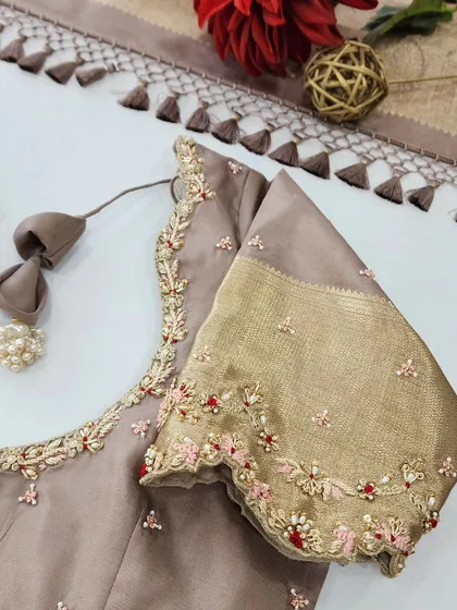 I love playing with different textures and colors. This elegant beige blouse features a sleeve made with a traditional gold silk border. The body of the blouse is adorned with delicate floral embroidery using pink and red threads, pearls, and stones for a subtle pop of color.