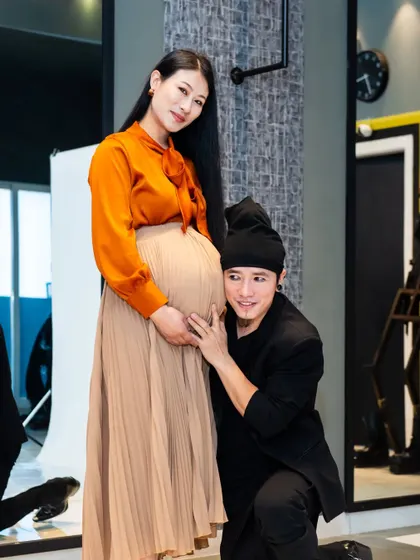 A behind-the-scenes glimpse of a studio maternity shoot. The father-to-be listens to the baby bump against a simple white backdrop, showing the setup for these classic portraits.