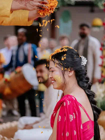 A close-up of the bride during the Haldi ritual, with marigold petals being showered on her head, her smile radiating pure joy.