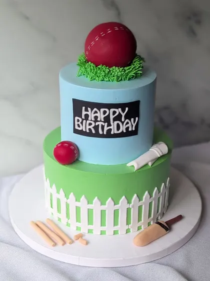 A true delight for a cricket enthusiast. This two-tier cake features a cricket pitch design with a picket fence, bat, ball, and wickets.