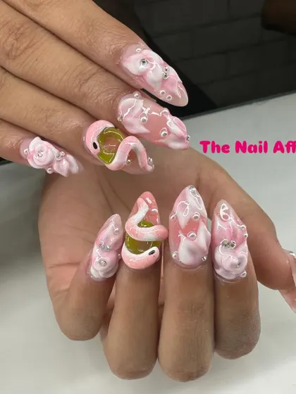 An example of our advanced sculptural work, these stiletto nails feature intricate 3D art, including a pink snake, textured bubbles, and rhinestone details for a dramatic and unique style.