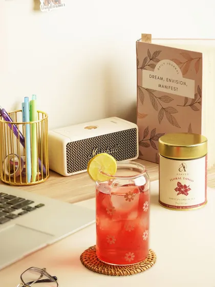 A cozy desk setup featuring a glass of floral iced tea, a journal, and a laptop, creating a scene of mindful work or relaxation.