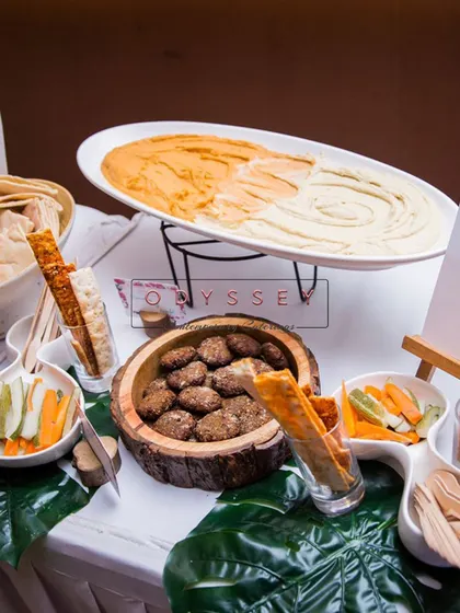 A Mezze platter featuring two types of hummus, falafel, and pita bread, presented on a bed of monstera leaves for a tropical, modern touch.
