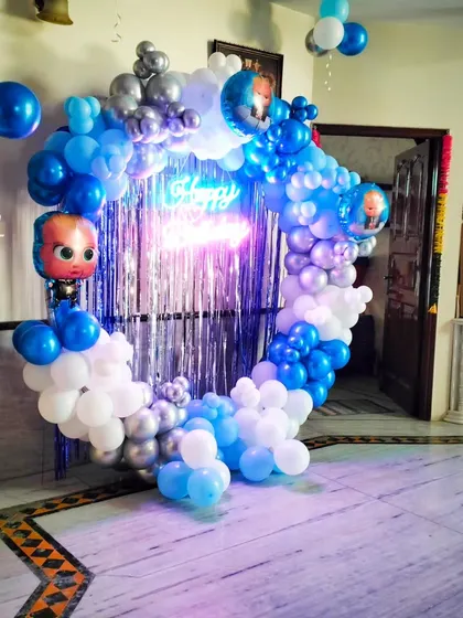A home-based Boss Baby themed birthday decoration. The circular balloon arch with a tinsel backdrop and neon sign is a great way to create a special party corner in any room.
