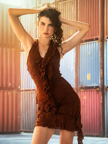 An industrial setting with shipping containers, created with projection. The warm lens flare adds a cinematic touch, contrasting the hard, industrial lines with the soft, flowing dress.
