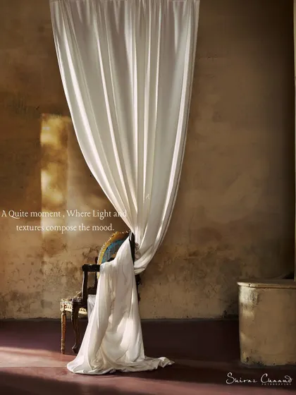 A quiet moment where light and texture compose the mood. The soft fabric contrasts with the rough, aged walls, creating a rich, tactile image for this textile campaign.