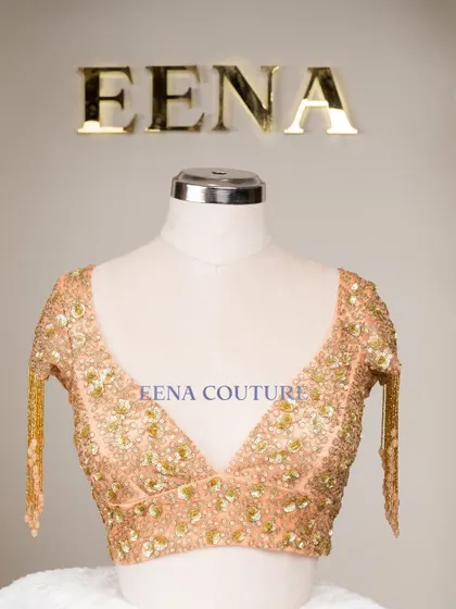 This peach-toned blouse is all about the sparkle and movement. It's crafted from net and covered in sequin and zardozi floral motifs, with dramatic, dangling beaded tassels on the sleeves for a show-stopping effect.