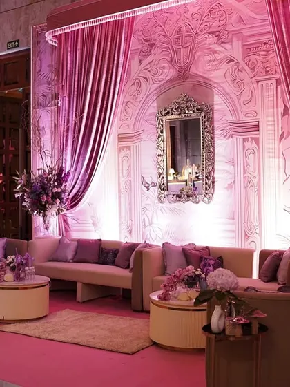 The soft pink lighting enhances the elegance of this lounge setup, with its curved sofas, rich purple cushions, and beautifully detailed architectural backdrop.