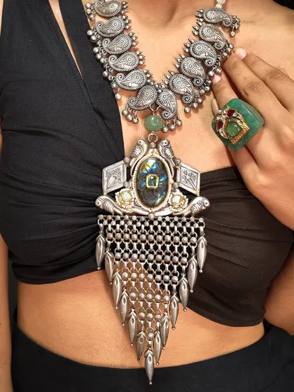A bold, layered look featuring two of our oxidized silver necklaces. The top piece has paisley motifs, while the bottom one is a statement pendant with a large central stone and silver mesh.