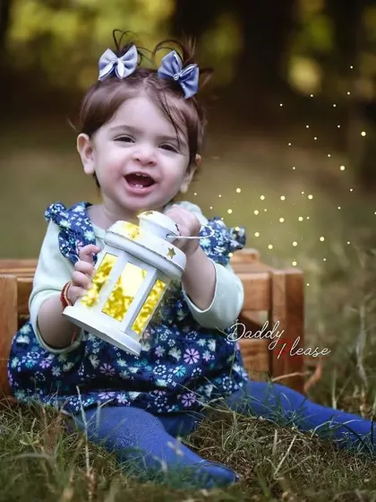 A magical outdoor portrait of a one year old girl sitting in the grass and holding a glowing lantern. The added sparkle effect makes the photo even more special.