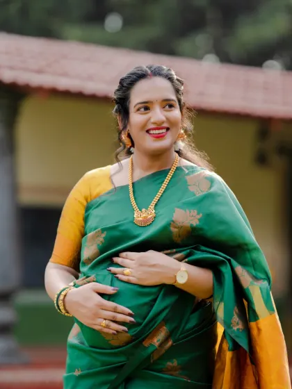 The joy of motherhood shines so brightly. This expecting mother looks radiant in a green and yellow silk saree, captured during a beautiful outdoor traditional maternity shoot.