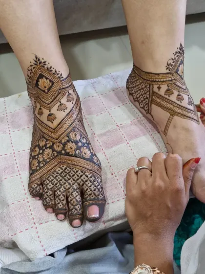 A work-in-progress shot of a modern V-shaped feet design, showing the artist's hand as she applies the delicate details.