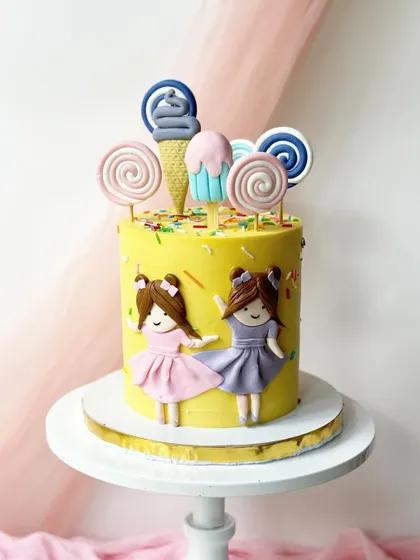 A bright and cheerful cake for two best friends. This yellow cake is decorated with sprinkles, lollipops, and two cute girl figurines.