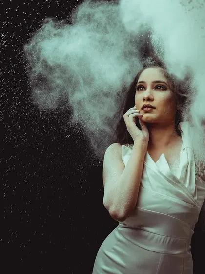 Model in a white dress against a black background, with a cloud of white powder exploding around her