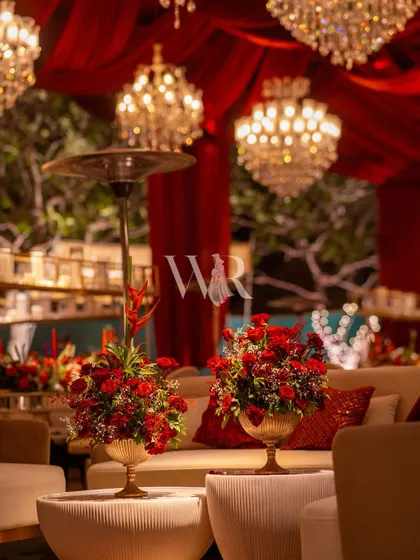 A close-up of the lounge seating, with the glow of the chandeliers reflecting off the modern furniture. The small bouquets of red roses in brass urns add a touch of color and luxury.