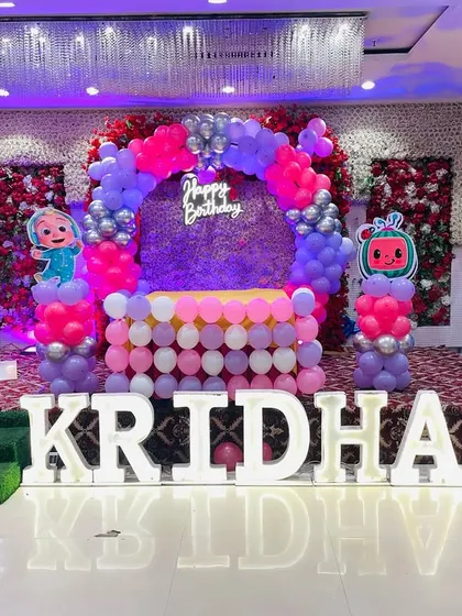 A wide view of a Cocomelon first birthday stage. This shows the full scale of the decoration, including the character cutouts, balloon arch, and illuminated name.