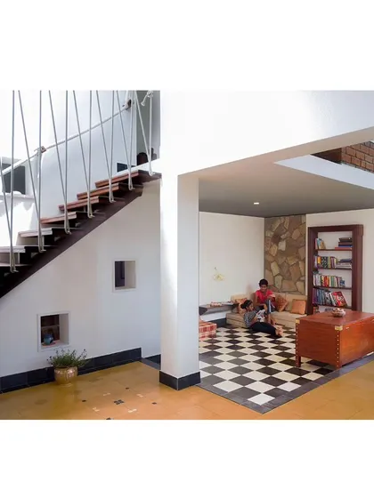 This sunken lounge area in 'Malenadu Mane' creates an intimate nook for conversation. The checkered flooring and built-in bookshelf add a classic touch to this cozy corner.