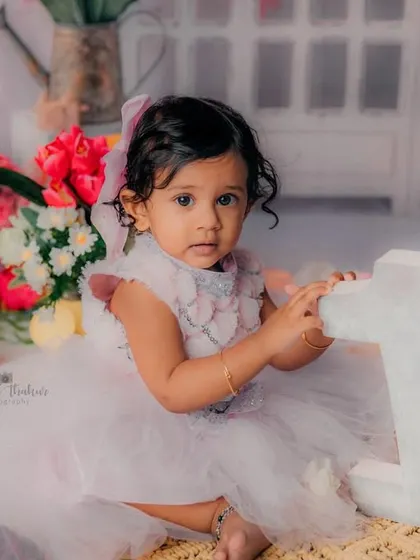 Posing with the number '1' to mark her special day. The soft colors and floral background create a beautiful setting for a first birthday.