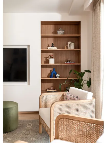 Clean lines, warm wood, and a palette of muted blues and greens define the living room. Here, a built-in shelf offers a place for curated objects, adding personality to the modern coastal design.