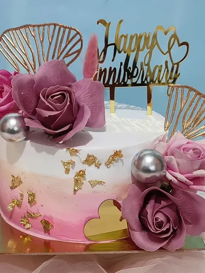 A square anniversary cake with a pink ombre effect, decorated with purple roses and gold accents.