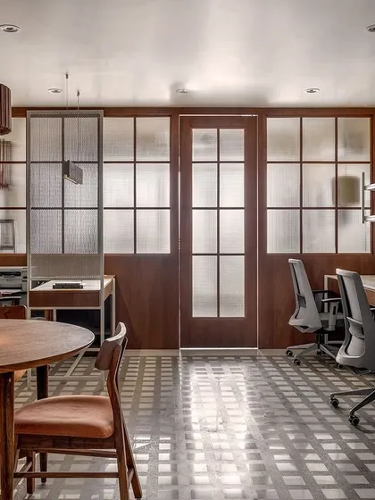 This view of the 'On The Grid' office showcases the open and organized environment we created. The workspace features shared desks with clean lines, separated from the meeting area by a perforated metal screen. A custom wooden pendant light adds a touch of warmth to the minimalist design.