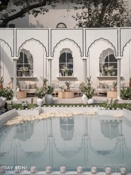 A serene poolside lounge area, where the reflection of the white arched pavilion in the water adds another layer of beauty to the scene.
