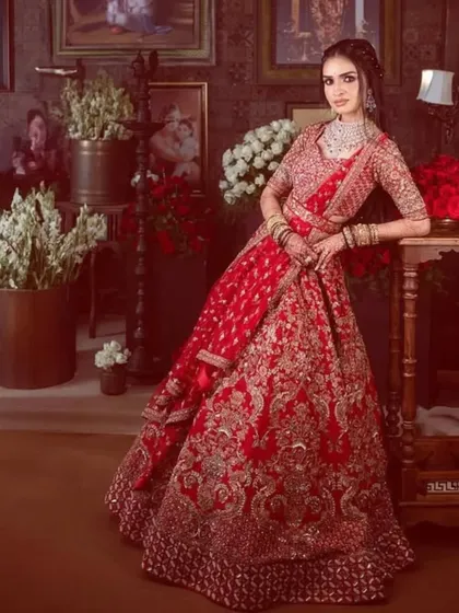 A full, regal portrait of the bride in her red reception lehenga. The rich colors and grand setting are matched by her confident and glamorous makeup.