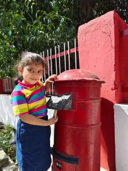 A student proudly posts her own letter in a traditional red postbox. This field trip sparked curiosity about the journey of a handwritten letter.