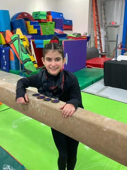 Camila, a Level 8 gymnast, proudly displays her medals after winning 1st on bars, 2nd on beam, and 1st on floor.