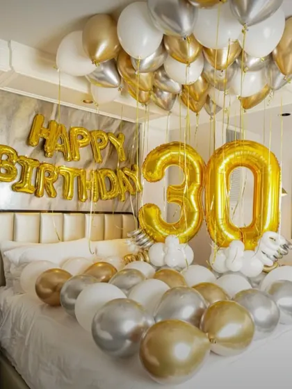 A luxurious 30th birthday bedroom setup with gold, silver, and white balloons, and large '30' foil numbers.