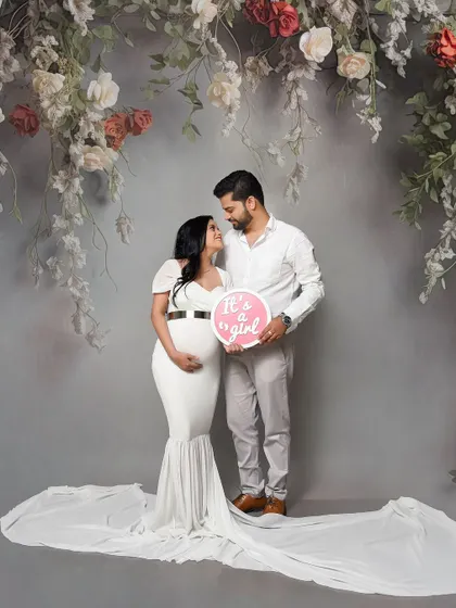 A sweet gender reveal portrait for a baby girl. The couple shares a happy moment under our floral arch, announcing the exciting news with a cute sign.
