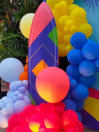 A close-up of the pool party decor, showing a custom surfboard prop surrounded by bright, summery balloons.