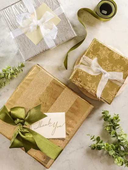 An elegant flat lay of gifts wrapped in gold and green paper from Crown Greetings. The "Thank You" card adds a personal touch, positioning the products as perfect for expressing gratitude.